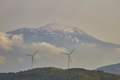 Two wind generators on a green hill, snow-capped Mount Etna in the background, Nebrodi National