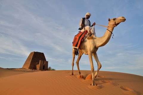 Man riding a dromedar in front of a pyramid of the northern cemetery of Meroe, Nubia, Nahr an-Nil,