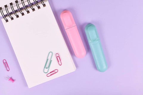 Clipboard with pink and blue text markers and paper clips on purple background with empty copy