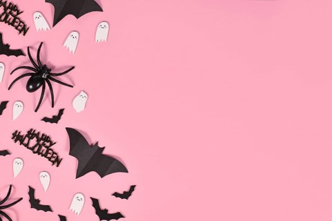 Halloween flat lay with bats, spiders, Happy Halloween text and cute ghosts on side of pink