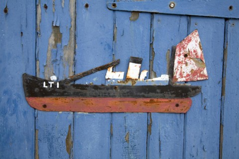 Old scrap metal model of ship on blue painted shed wall, Felixstowe Ferry, Suffolk, England, UK