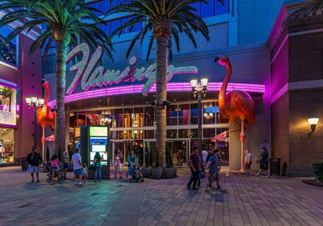 Tourists walking past the purple and pink neon lights at the entrance to the Flamingo Las Vegas