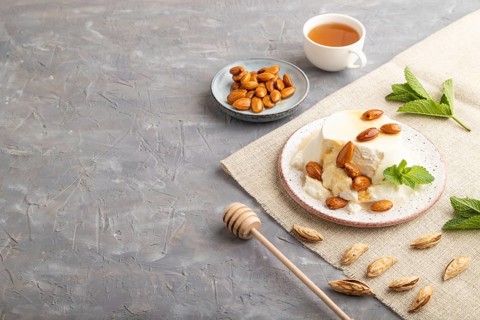 Ricotta cheese with honey and almonds on gray concrete background and linen textile. side view,