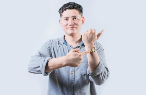 Smiling young man pointing at his wrist watch isolated. Portrait of person pointing his wrist watch