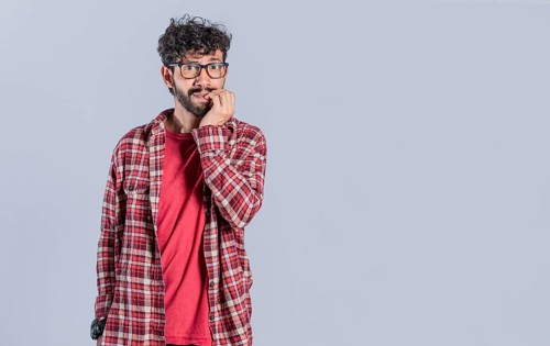 Nervous young man with worried expression bites nails and looks anxiously isolated