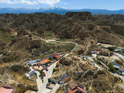 Mountain village with scattered houses and rocky landscape in the foreground, in a sunny valley
