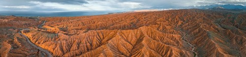 Panorama, landscape of eroded hills, badlands at sunset, behind mountain peaks of the Tian Shan