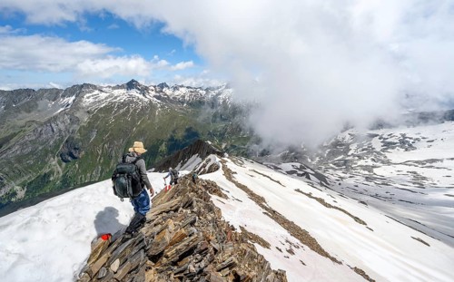 Mountaineer on a rocky ridge with snow, descent from the summit of Schönbichler Horn, view of