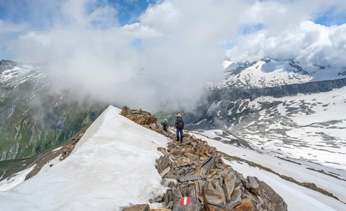 Mountaineer on a rocky ridge with snow, descent from the summit of Schönbichler Horn, view of