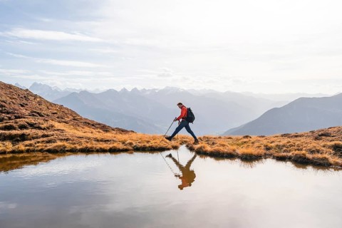 Mountaineer hiking with poles, reflected in a small mountain lake on the Krahberg, mountain