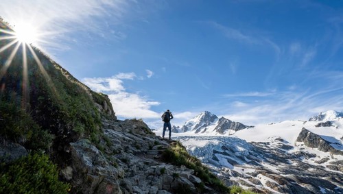Mountaineer in front of high alpine mountain landscape with sun star, summit of Aiguille de