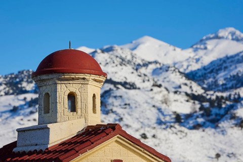Close-up of a church tower with a red roof in the snowy mountains under a clear sky, Lefka Ori,