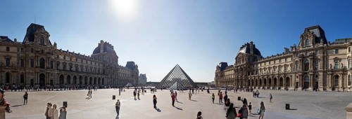 Panoramic view of the Louvre with the glass pyramid and numerous visitors under a clear sky, Paris