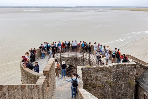 A group of people stand on a viewing platform overlooking the sea and surrounded by historic walls,