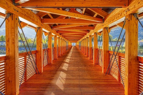 View along an illuminated wooden bridge with a view of the mountains and river, Inn footbridge,