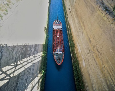 Aerial view of a red ship travelling through a narrow channel under a bridge, Corinth Canal,
