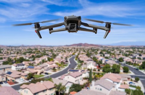 Unmanned aircraft system (UAV) quadcopter drone in the air over residential neighborhood.
