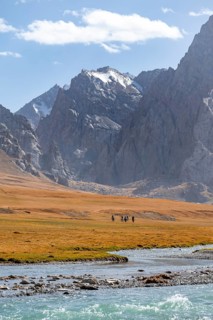 Rider in mountain landscape with yellow meadows, river Kol Suu and mountain peaks with glacier,