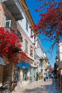 A picturesque, sunny alley with historic buildings and flowering red plants, Nafplio, Nauplia,