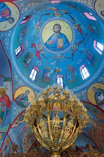 Religious icons and frescoes adorn a blue domed ceiling with a golden chandelier, Church of the