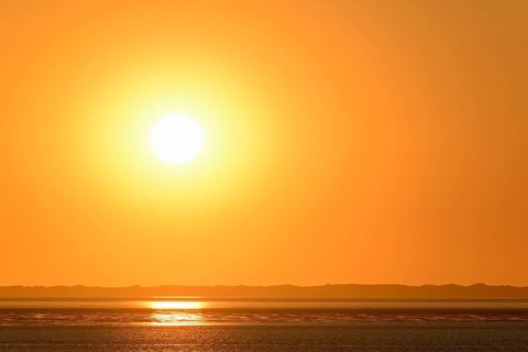 Sunset over the North Sea at low tide, the outline of the island of Juist on the horizon,