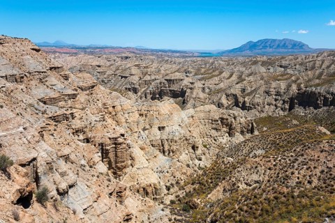 Large canyon area with rock formations and bare vegetation under a bright blue sky, Barranco de la