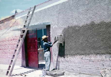 Construction worker throwing cement through a sieve to make wall panelling over modern red bricks,