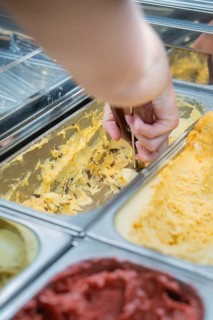 A hand scoops yellow ice cream out of a metal box with an ice cream scoop, Autumn creations at Cafe