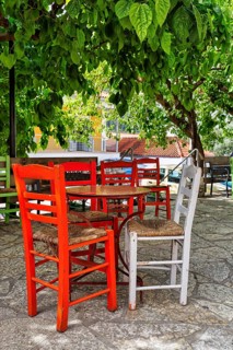 Terrace under trees, table and red chairs in front of a café, small town Leonidio, Tsakonia,