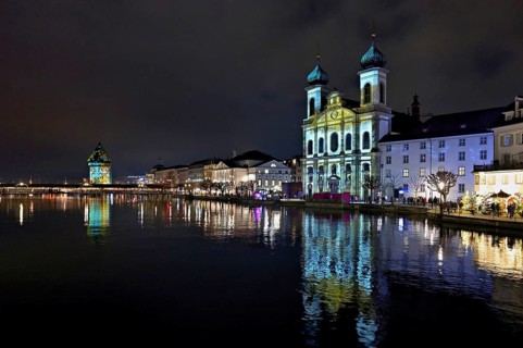 Water tower and Jesuit church on the right with light installation, on the Reuss at dusk, Old Town,