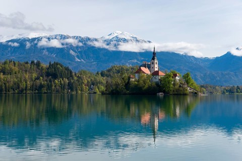 Church on an island, reflected in the calm lake, with mountain scenery in the background, Bled