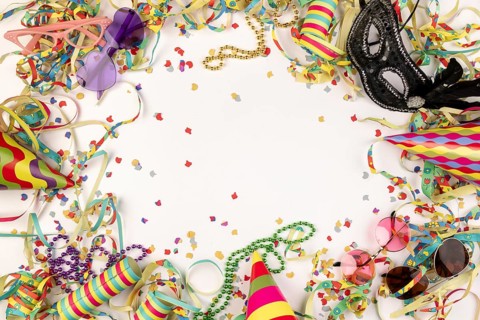 Colourful carnival paraphernalia such as hats, masks and confetti on a white background