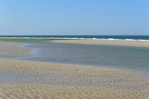 Beach at low tide with wave-like structure, current ripples in wet sand, blue sky, North Sea,
