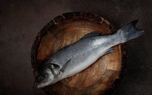 Fresh, raw sea bass fish, in a wooden plate, top view, no people.