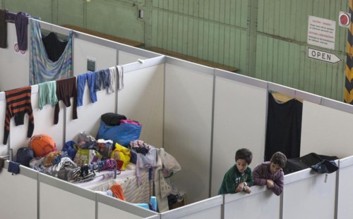 Children of refugees look over the wall of a temporary room in an emergency shelter for refugees on