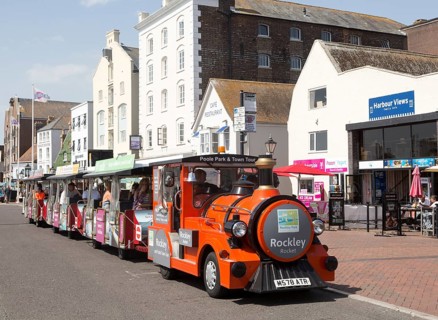 Rockley Rocket land train passing old historic buildings on quayside at Poole harbour, Poole,