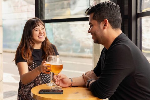 Man and woman enjoying beer in a bar during the day. She is laughing, making it evident that they