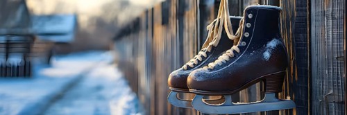 Pair of vintage ice skates hanging by their laces on an old wooden fence with frost and snow gently