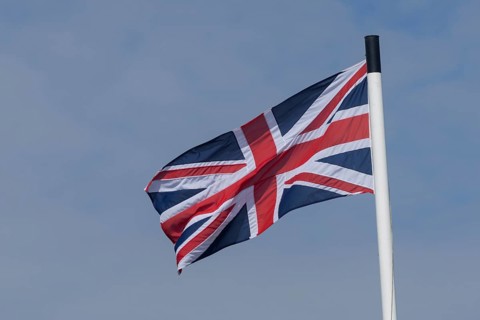 Union jack flag of the United Kingdom blowing in the wind against a blue sky, England, United
