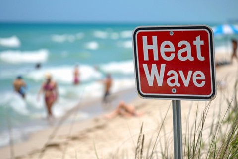 Sign with text 'Heat wave' in front of blurry sunny beach with people. KI generiert, generiert, AI