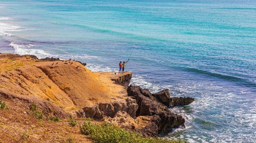 Anglers stand on the cliff at Mughsail Beach on the Arabian Sea, near Salalah, Dhofar Province,