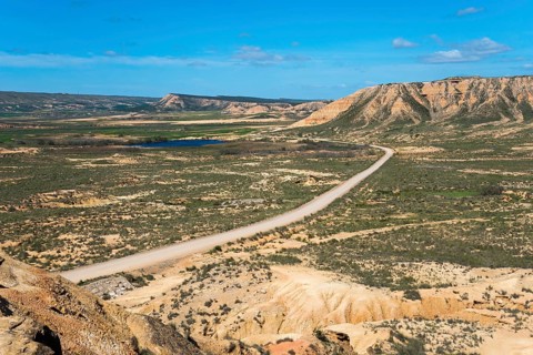 Wide landscape with a long road and hills under a clear blue sky, Bardenas Reales Natural Park,