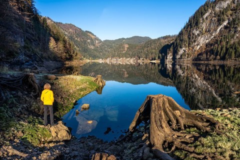 The Vordere Gosausee in autumn with a view of the Gasthof Gosausee. A hiker stands by the lake. A