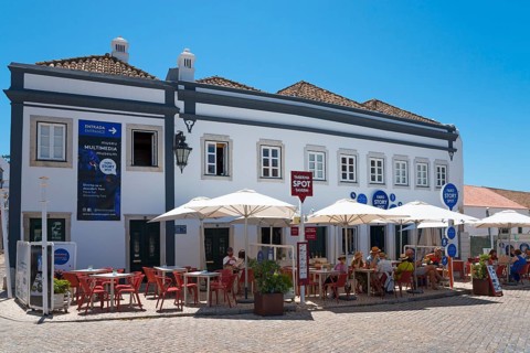 Café with umbrellas and guests outside in front of a blue-painted building on a sunny day, Faro