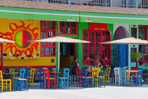 A lively street bar with colourful chairs and a colourful façade, guests under parasols, Sarti,