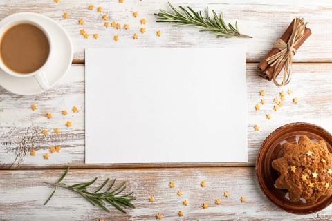 White paper sheet mockup with cup of coffee and cake on white wooden background. Blank, top view,