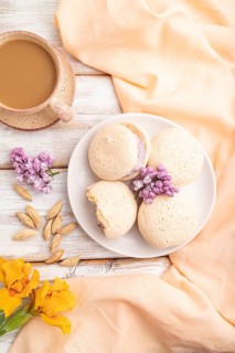Meringues cakes with cup of coffee on a white wooden background and orange linen textile. Top view,