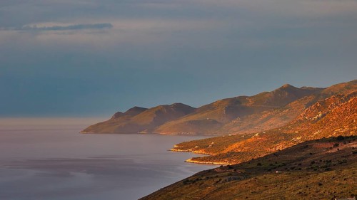 Golden morning sun illuminates a coastal landscape with mountains and sea, Mani Peninsula,