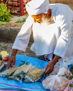 An elderly Omani man in traditional dress offers his wares on the street, weekly market market in