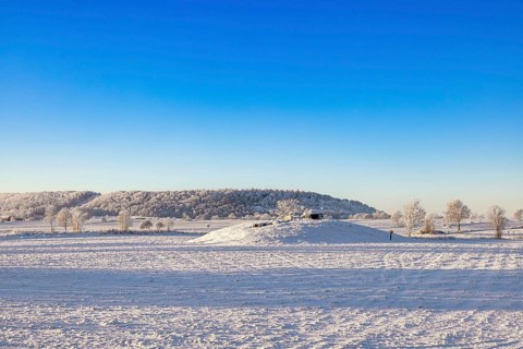 Passage grave from the stone age on a hill at a snowy field in a cold winter landscape at the